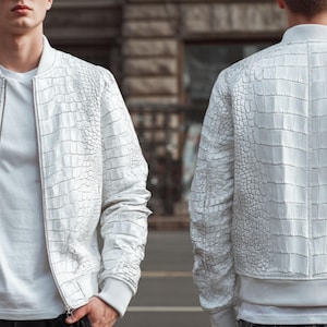 Op de afbeelding: Witte bomberjack met een getextureerd, krokodilachtig patroon. De jas heeft een ritssluiting, geribde manchetten en een geribde zoom. Er wordt een wit T-shirt onder gedragen. De jas wordt van voren en van achteren getoond.