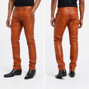 Puede incluir: Un pantalón de corte ajustado en un vibrante color naranja quemado con un patrón texturizado de piel de cocodrilo. El pantalón incluye una cintura estándar con trabillas, cierre de botón frontal, bolsillos laterales y dos bolsillos traseros.