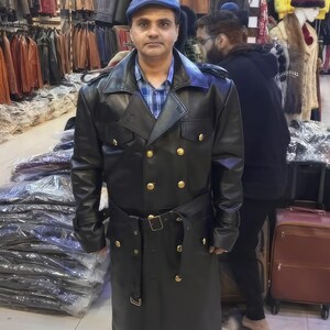 May include: A black leather trench coat featuring a double-breasted front with gold-toned buttons, a wide collar, shoulder epaulets, and a matching waist belt with a buckle. The coat has long sleeves with buckled cuffs and a long hemline.