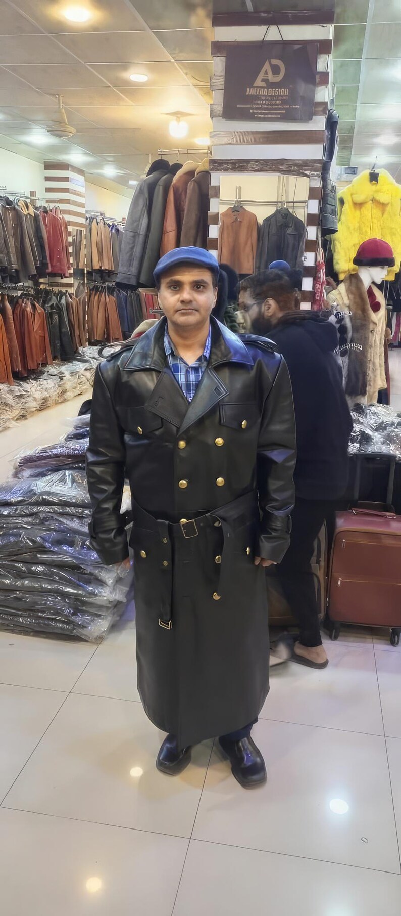 May include: A black leather trench coat featuring a double-breasted front with gold-toned buttons, a wide collar, shoulder epaulets, and a matching waist belt with a buckle. The coat has long sleeves with buckled cuffs and a long hemline.