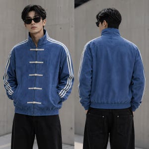 May include: A blue corduroy jacket featuring a high collar, long sleeves with three white stripes, and a front closure with five white toggle buttons. The jacket has a ribbed hem and cuffs, providing a structured fit with a textured fabric finish.