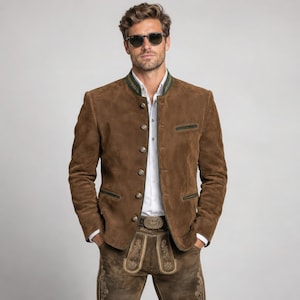 May include: A brown suede jacket with a stand-up collar, featuring dark green trim, a button-front closure, and two side pockets. The jacket is worn over a white button-down shirt, paired with brown leather trousers featuring decorative embroidery.