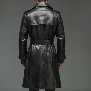 May include: A black leather trench coat featuring a wide collar, shoulder epaulets, and a belted waist. The coat has long sleeves with buckled cuffs and a back storm flap, extending to a mid-calf length with a clean, polished finish.