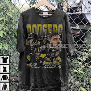 May include: A black t-shirt with a distressed design, displaying the word "RODGERS" in yellow block letters. The shirt features images of football players in black and gold uniforms. The word "AARON" is also visible.