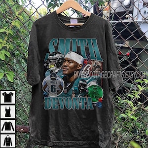 Puede incluir: Camiseta negra con un gráfico del jugador de fútbol americano Devonta Smith. El diseño incluye el nombre "SMITH" en letras turquesas, junto con imágenes de Smith con su uniforme de fútbol. También es visible el número "6".