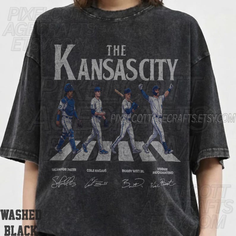 May include: Washed black t-shirt featuring a graphic of four baseball players crossing a crosswalk, with "The Kansas City" above. Player names and signatures are below. The shirt has a vintage, distressed look.