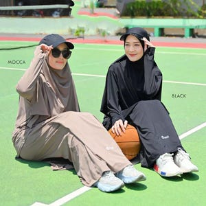Peut inclure: Deux femmes portant des tenues de sport modestes assorties sur un court de tennis. L'une est couleur mocca, l'autre noire. Les deux tenues comprennent une casquette, des lunettes de soleil et des baskets. Un ballon de basket est entre elles.