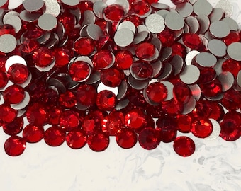 May include: A pile of red rhinestones with silver backing. The rhinestones are small and round, and they are scattered on a white surface.