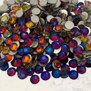 May include: A large pile of iridescent glass rhinestones in shades of blue, purple, orange, and red. The rhinestones are flat-backed and have a silver backing.