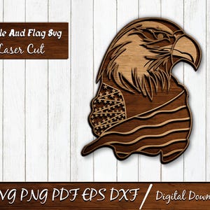 Op de afbeelding: Een houten lasergesneden ontwerp van een adelaarskop met de Amerikaanse vlag verwerkt in het ontwerp. De adelaar is bruin met gedetailleerde veren. De vlag heeft sterren en strepen. De tekst "Eagle And Flag Svg Laser Cut" wordt weergegeven.