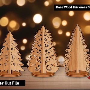 Op de afbeelding: Drie lasergesneden houten kerstbomen met ingewikkelde ontwerpen. De bomen zijn gemaakt van lichtgekleurd hout en staan op ronde voetstukken. De tekst "Base Wood Thickness 3mm" en "Laser Cut File" zijn zichtbaar. De achtergrond heeft vage bokeh-lichten.