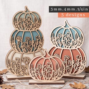 May include: Three laser-cut wooden pumpkin decorations with floral cutouts, featuring stacked and individual designs in blue, cream, and orange tones. Text on the image reads 3 mm, 4 mm, 1/4 in and 3 designs, indicating material thickness.