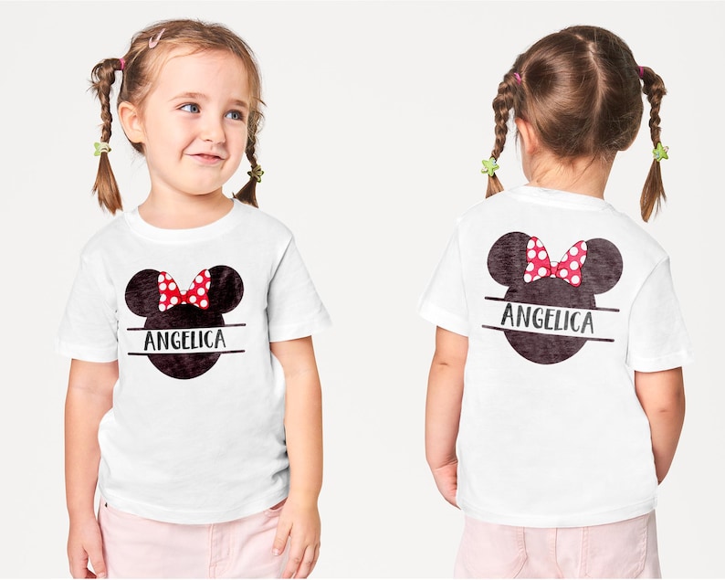 May include: White t-shirt featuring a Minnie Mouse design with a red polka dot bow and the name "Angelica" in black. The design is on the front and back of the shirt. The child is wearing pink pants.