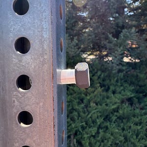 Peut inclure: Gros plan sur un poteau m&eacute;tallique rectangulaire et us&eacute;, perc&eacute; de trous circulaires espac&eacute;s. Un gros boulon hexagonal est fix&eacute; au poteau avec une entretoise blanche. Le poteau a un aspect rouill&eacute;, sugg&eacute;rant une utilisation en ext&eacute;rieur.
