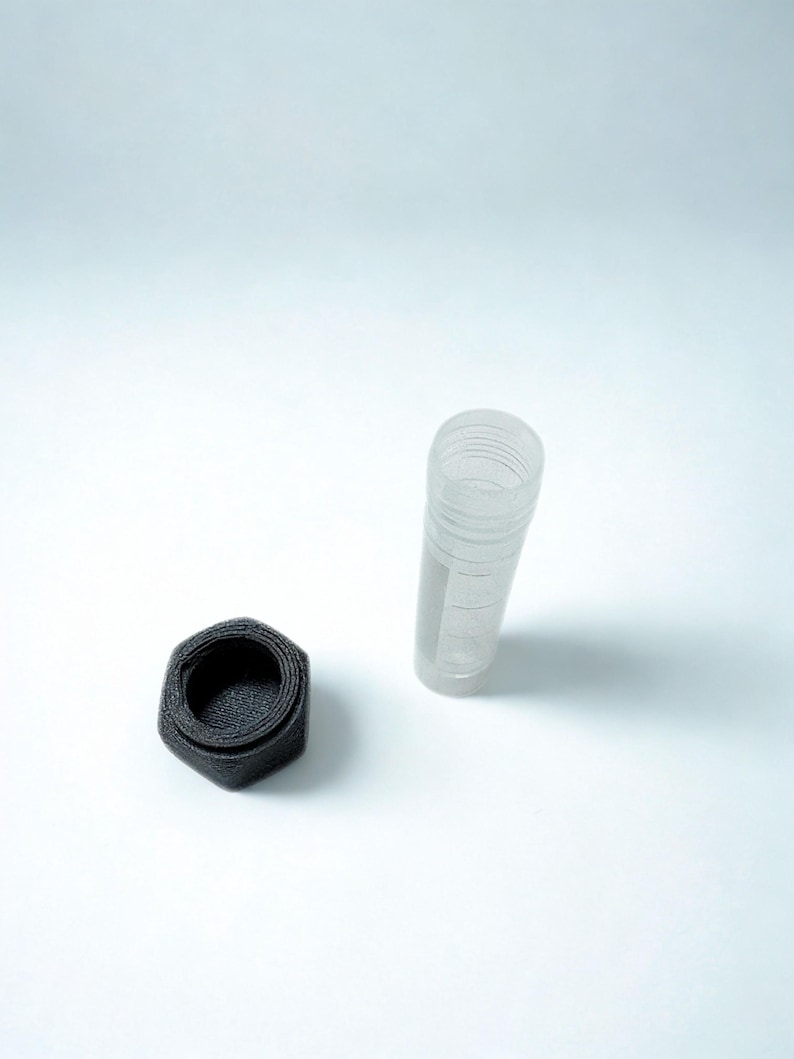 Peut inclure: Un r&eacute;cipient cylindrique transparent avec un design nervur&eacute; et un couvercle hexagonal noir s&eacute;par&eacute;. Le r&eacute;cipient est transparent et le couvercle est noir mat fonc&eacute;. Les articles sont pos&eacute;s sur un fond blanc uni.
