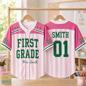 May include: A pink and white vertical striped baseball jersey with green trim. The front features the text FIRST GRADE and Mrs. Smith with two green stars. The back displays the name SMITH and the number 01 in large green block lettering.