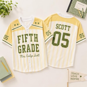 May include: Two baseball-style jerseys with yellow and white vertical stripes. The front features the text FIFTH GRADE and Mrs. Evelyn Scott in green. The back displays the name SCOTT and the number 05 in large green block lettering.