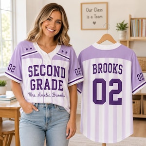 May include: A light purple and white vertical striped baseball jersey featuring the text SECOND GRADE and Mrs. Amelia Brooks on the front, with the number 02 and two stars on each sleeve. The back displays the name BROOKS and the number 02.