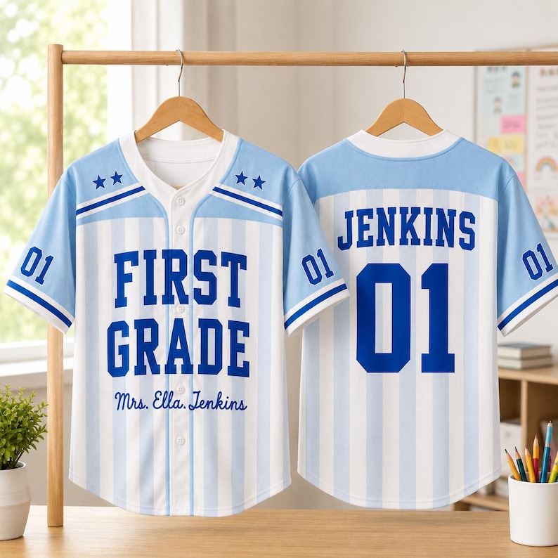 May include: A light blue and white vertical striped baseball jersey with a button-down front. The front features the text "FIRST GRADE" and "Mrs. Ella. Jenkins" with two stars on each shoulder. The back displays the name "JENKINS" and "01".