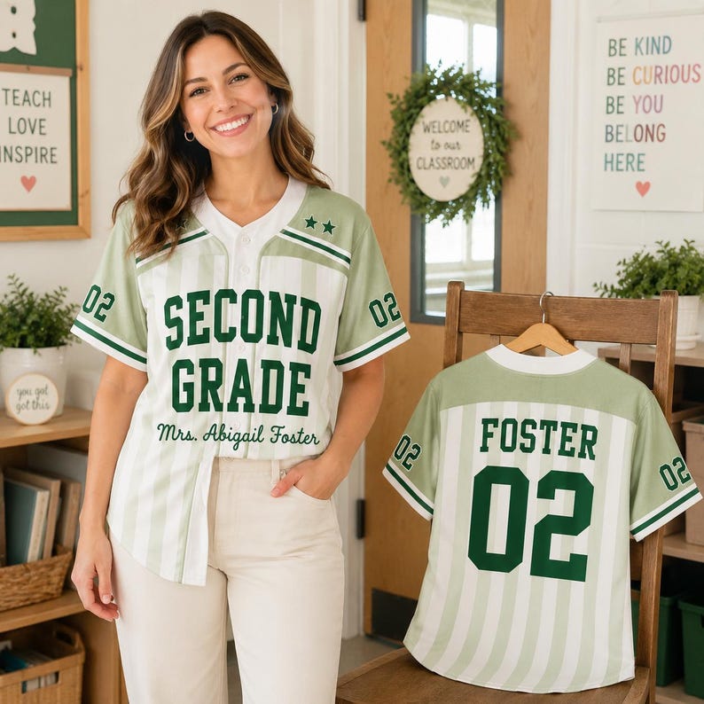May include: A sage green and white striped baseball jersey featuring the text SECOND GRADE and Mrs. Abigail Foster on the front, with the name FOSTER and the number 02 on the back. The shirt has a white V-neck collar and green sleeve trim.