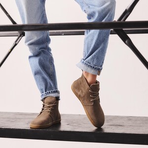 Puede incluir: Botines de ante marr&oacute;n con dise&ntilde;o de cordones y suela de goma. Las botas se llevan con vaqueros de mezclilla azul claro. Las botas parecen ser de un color neutro, adecuado para varios atuendos.