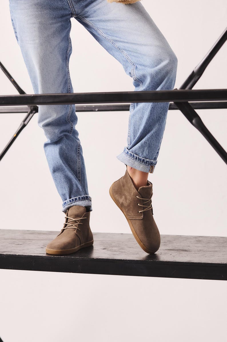 Puede incluir: Botines de ante marr&oacute;n con dise&ntilde;o de cordones y suela de goma. Las botas se llevan con vaqueros de mezclilla azul claro. Las botas parecen ser de un color neutro, adecuado para varios atuendos.