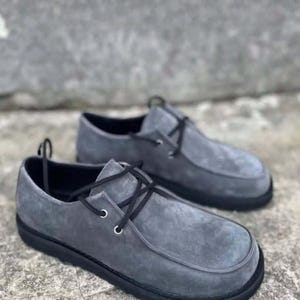 Pu&ograve; includere: Un paio di scarpe grigie in camoscio con lacci neri e suole nere. Le scarpe hanno un design a punta arrotondata e uno stile casual, adatto all'uso quotidiano.