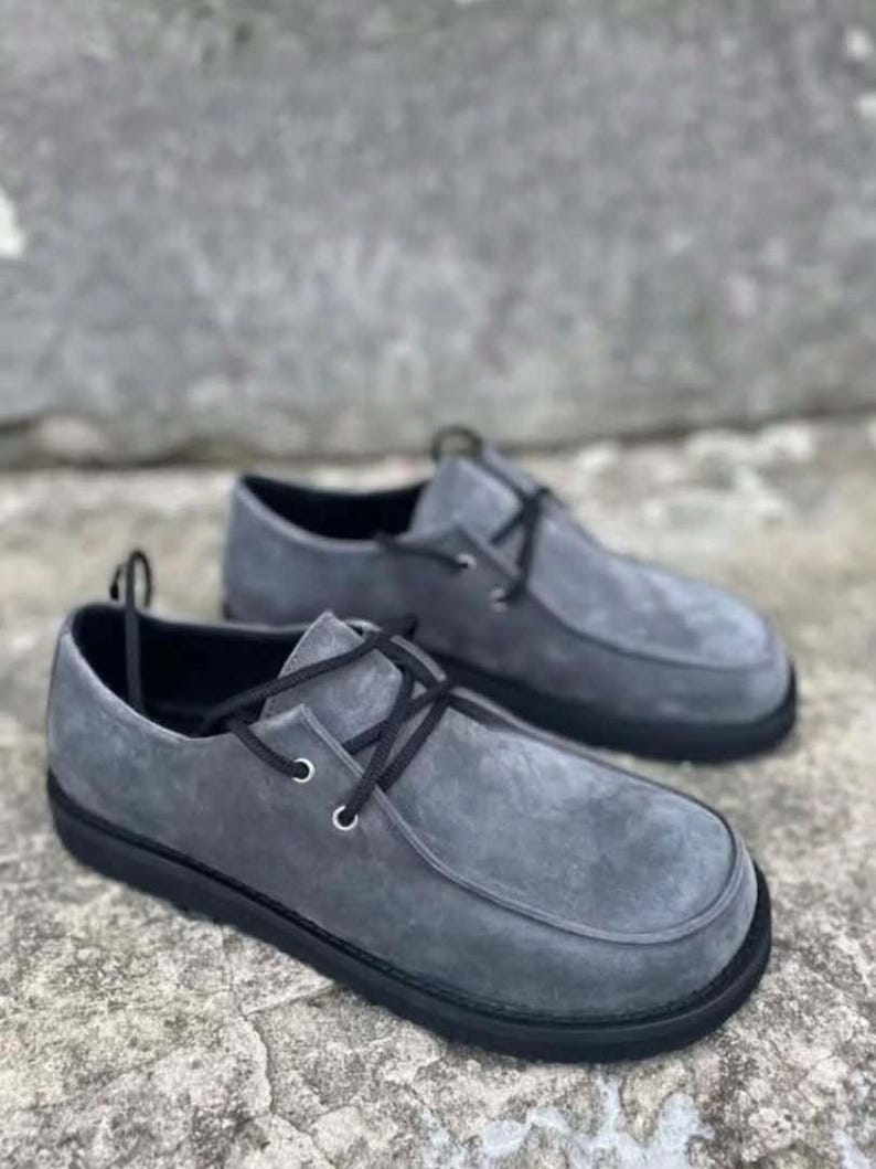 Pu&ograve; includere: Un paio di scarpe grigie in camoscio con lacci neri e suole nere. Le scarpe hanno un design a punta arrotondata e uno stile casual, adatto all'uso quotidiano.