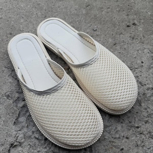May include: A pair of off-white mesh slip-on shoes. The shoes have a rounded toe and a thick, light-colored sole. The upper part of the shoe is made of a mesh material, and the interior is a solid, smooth material.