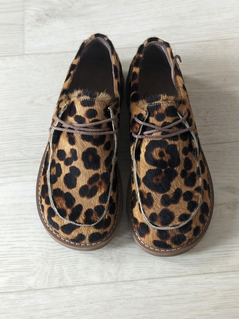 Pu&ograve; includere: Un paio di scarpe slip-on con stampa leopardata. Le scarpe hanno una suola marrone e un motivo maculato marrone e nero. Le scarpe hanno lacci marroni e un bordo cucito intorno alla suola.
