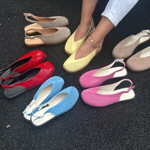 May include: A collection of colorful women's flats in various shades, including red, blue, pink, yellow, and beige. The shoes feature a perforated design and slingback straps. The flats are displayed on a dark surface.