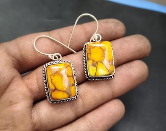 May include: A pair of rectangular earrings with a silver-colored metal setting. Each earring features a yellow and brown stone with a unique pattern. The earrings have a hook closure.