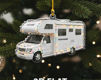May include: A white camper ornament with the text "YOUR NAME" and "2D FLAT". The camper is decorated with colorful string lights and is hanging from a gold string. The ornament is set against a blurred background of Christmas tree branches and lights.