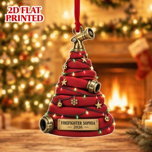 Puede incluir: Un adorno de árbol de Navidad impreso en plano 2D con forma de manguera de incendio roja enrollada con boquillas y conectores de color latón metálico. El adorno presenta pequeños dijes de estrellas y copos de nieve dorados, luces y una placa que dice FIREFIGHTER SOPHIA 2026.