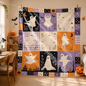 May include: A square quilt featuring a grid of nine panels, each displaying a white ghost performing ballet poses. The background panels alternate between orange, purple, black, and white checkered patterns, decorated with pumpkins, bats, and flowers.