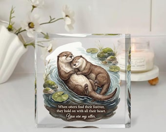 May include: A clear, square block featuring a watercolor illustration of two otters embracing in a pond. The text reads, "When otters find their forever, they hold on with all their heart. You are my otter."