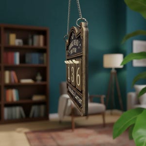 Puede incluir: Contador de libros de madera con el texto "Books Read This Year" y el n&uacute;mero "136". El contador est&aacute; colgado de una cadena plateada. El fondo incluye una estanter&iacute;a, una l&aacute;mpara y una silla.