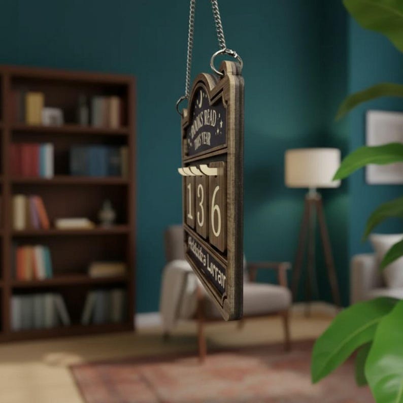 Puede incluir: Contador de libros de madera con el texto "Books Read This Year" y el n&uacute;mero "136". El contador est&aacute; colgado de una cadena plateada. El fondo incluye una estanter&iacute;a, una l&aacute;mpara y una silla.