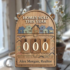 May include: Wooden sign with the text "HOMES SOLD THIS YEAR" and a row of colourful houses. Below are three wooden number blocks displaying "000". The sign includes the name "Alex Morgan, Realtor".