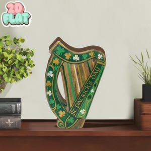 May include: Wooden harp decoration with green, gold, and brown accents. The harp features shamrock and floral designs, with the text "St. Patrick's Day" on the side. The harp is displayed on a wooden surface.