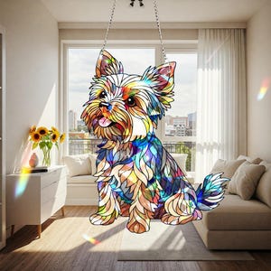 May include: A colorful stained glass Yorkshire Terrier dog decoration, hanging from a silver chain. The dog features a variety of colors including blue, yellow, orange, and green. The dog is sitting with its tongue out.