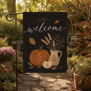 May include: A black garden flag featuring the word welcome in white cursive script. The design includes a large orange pumpkin, a smaller white pumpkin, and a cream-coloured pitcher filled with wheat stalks and autumn leaves on a dark background.