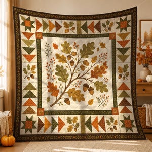 Op de afbeelding: Een vierkante quilt met een centraal crèmekleurig paneel met een print van eikenbladeren en eikels in tinten groen, oranje en bruin. De rand bestaat uit geometrische driehoeks- en sterpatronen in bijpassende herfstkleuren.