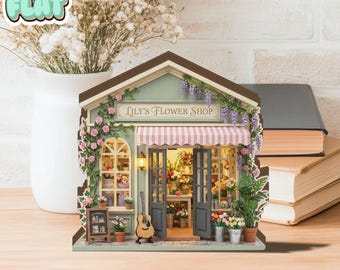 May include: A miniature flower shop model with the text "Lily's Flower Shop" above the entrance. The shop has a green facade, a striped awning, and is decorated with flowers and vines. A guitar leans against the shop, and a small chalkboard sign is visible.