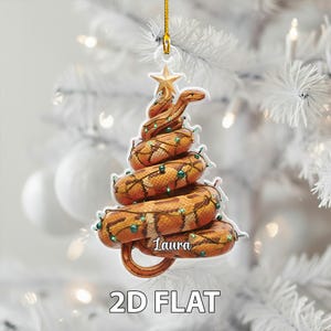Könnte beinhalten: Ein einzigartiger Weihnachtsbaumschmuck in Form einer Schlange, verziert mit Lichterketten und einem Stern. Die Schlange ist braun und orange mit einem Schuppenmuster, und die Lichter sind grün. Der Name "Laura" steht auf dem Ornament. Der Text "2D FLAT" steht unten.