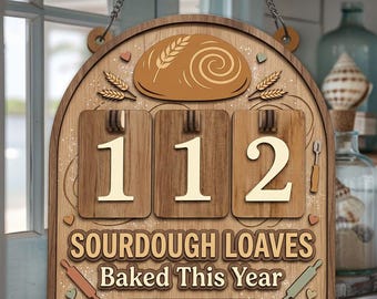 May include: Wooden sign with a bread loaf illustration, wheat stalks, and the numbers "112." Text reads "Sourdough Loaves Baked This Year" and "Emma's Bake Log." Includes rolling pin and heart accents. Hanging chain at the top.