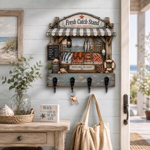 Peut inclure: Un porte-clés mural en forme d'étal de poissonnerie avec un auvent rayé bleu et blanc, un tableau noir et des miniatures de fruits de mer. Il comporte quatre crochets en métal noir, dont un supportant un trousseau de clés sur le deuxième crochet.
