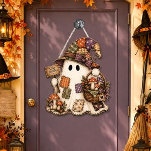 May include: A hanging wall sign shaped like a ghost wearing a patchwork hat, holding a sign that reads stay spooky in one hand and a woven basket filled with mushrooms in the other. The ghost features various fabric-style patches.