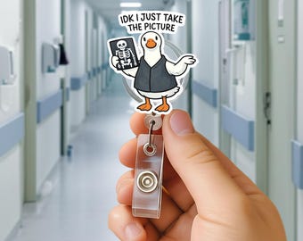 May include: A white and black goose cartoon badge reel with the text "IDK I JUST TAKE THE PICTURE". The goose is wearing a vest and holding an x-ray. The reel has a clear plastic strap and a metal button.