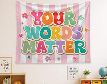 May include: A wall tapestry featuring a pink and white vertical striped background with the text YOUR WORDS MATTER in large, colorful, bubble-style letters. The design is decorated with small flowers, hearts, and stars in various pastel colors.